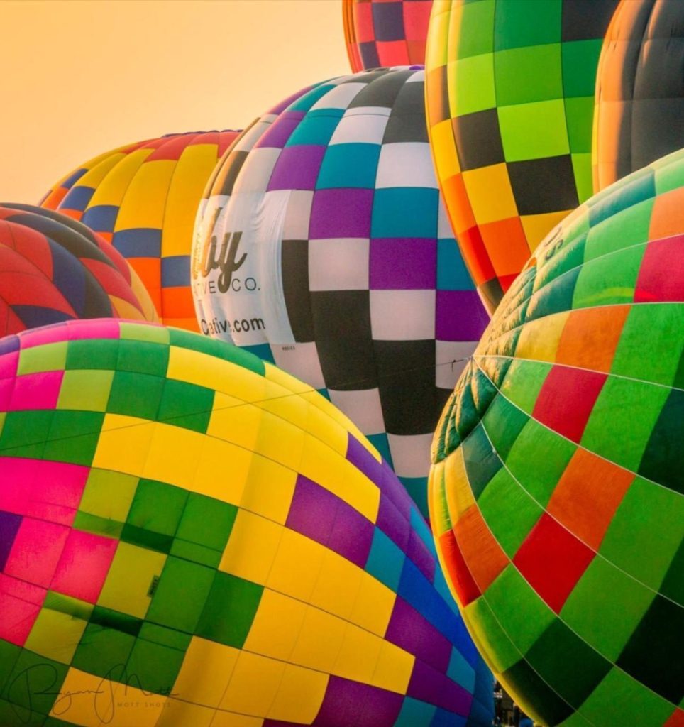 Brightly colored hot air balloons with a checkered pattern are clustered together, filling the frame against a warm sky at sunrise or sunset.